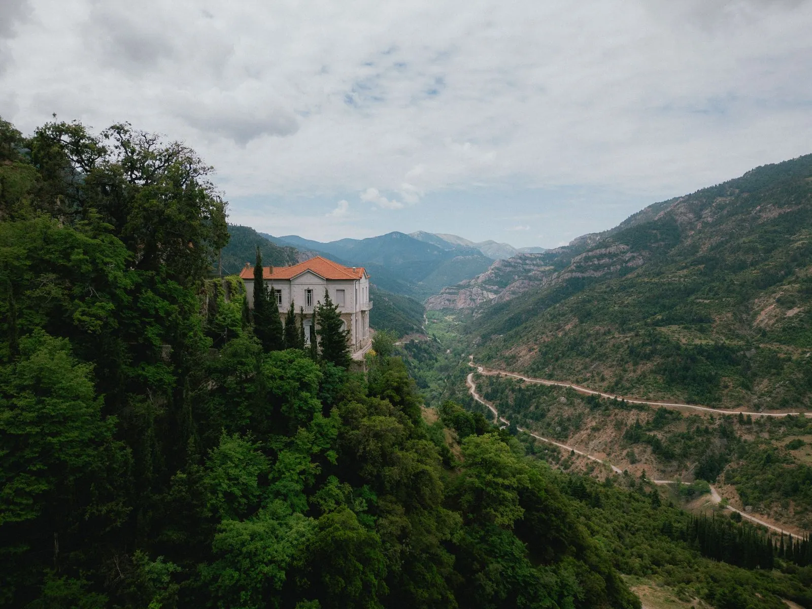 Το κτίριο του ξενώνα ανάμεσα στα δέντρα, με το φαράγγι και τον δρόμο από κάτω